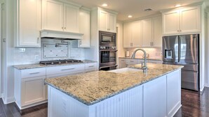 Una cocina moderna con armarios blancos, electrodomésticos de acero inoxidable, encimeras de granito y una isla central.