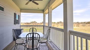 Relax on the covered porch with a table and four chairs, surrounded by a tranquil view of a grassy field and distant trees.