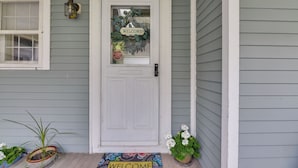 Una puerta principal con un letrero que dice 'WELCOME', una señal de stop y plantas en macetas.