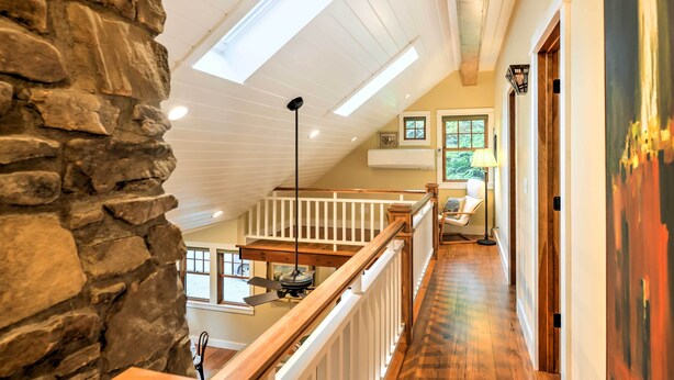 A spacious loft with a high ceiling, skylights, a wooden staircase, and a view of the outdoors.