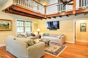 A spacious living room with a large sectional sofa, a television mounted on the wall, and a wooden ceiling with exposed beams. - 'sugar Berry' Craftsman Home in Laughlintown (Laughlintown)