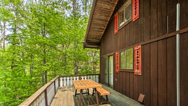 Une terrasse en bois avec une table de pique-nique et des bancs, entourée d’une rambarde, donnant sur une zone boisée.