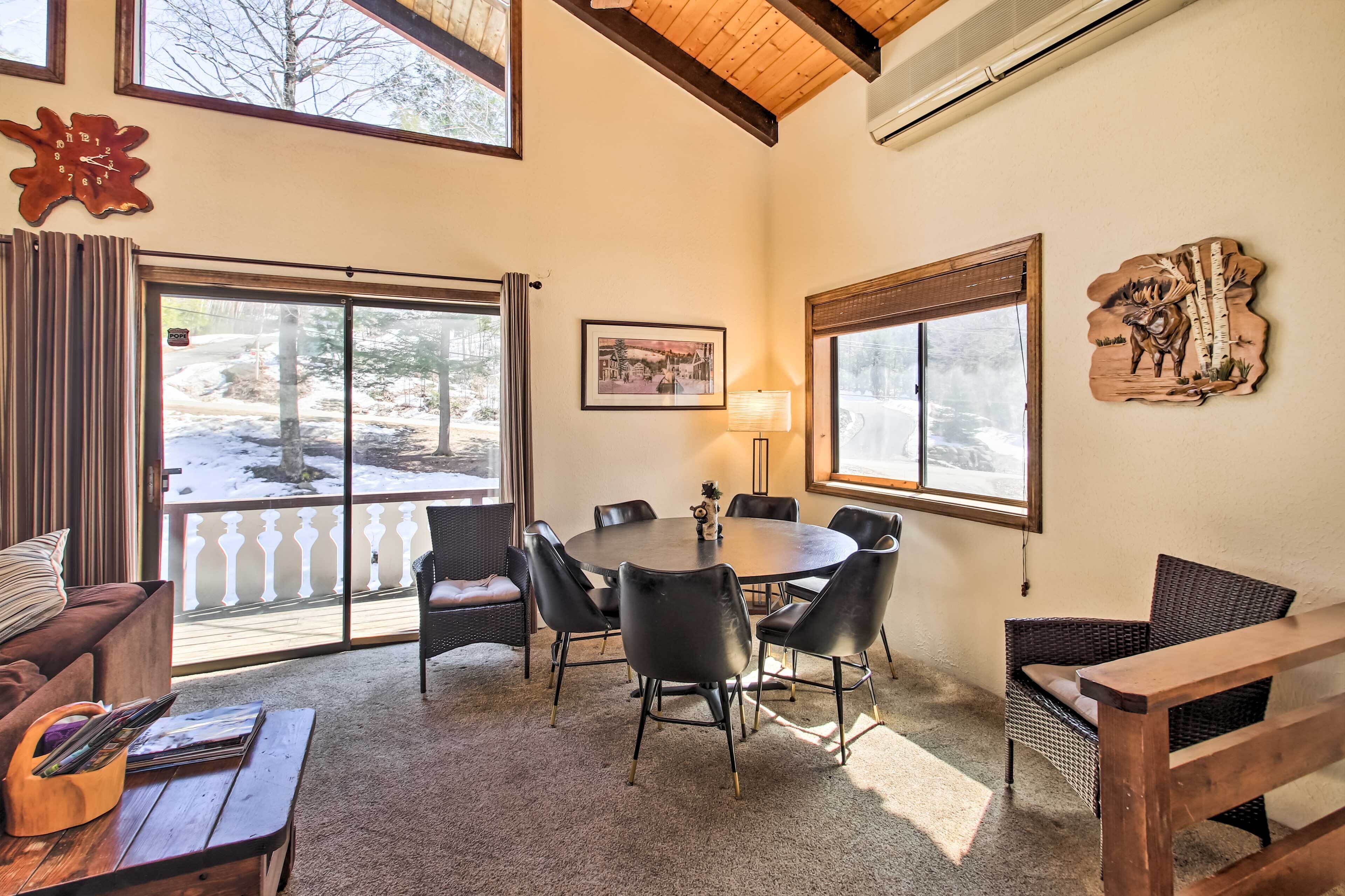 A cozy room with a round table, black chairs, a wooden bench, and a large window with a view of a snowy landscape.