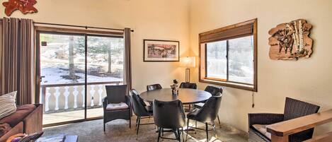 A cozy room with a round table, black chairs, a wooden bench, and a large window with a view of a snowy landscape.