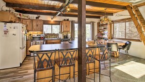 Cocina rústica con vigas de madera, una isla central con taburetes de bar y un comedor con lámpara de araña.