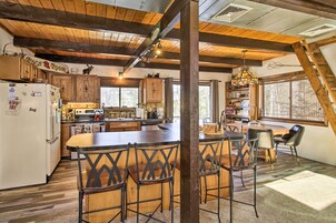 Cocina rústica con vigas de madera, una isla central con taburetes de bar y un comedor con lámpara de araña.