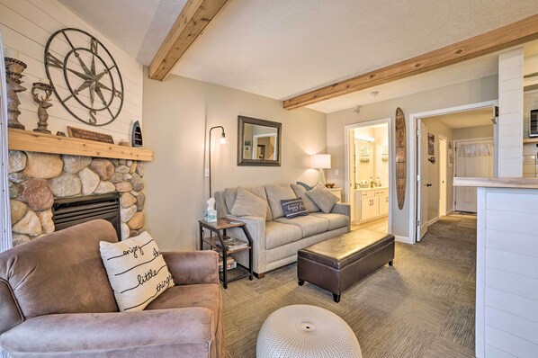 A cozy living room with a stone fireplace, a large wall clock, and a comfortable seating area with a sofa and ottoman.