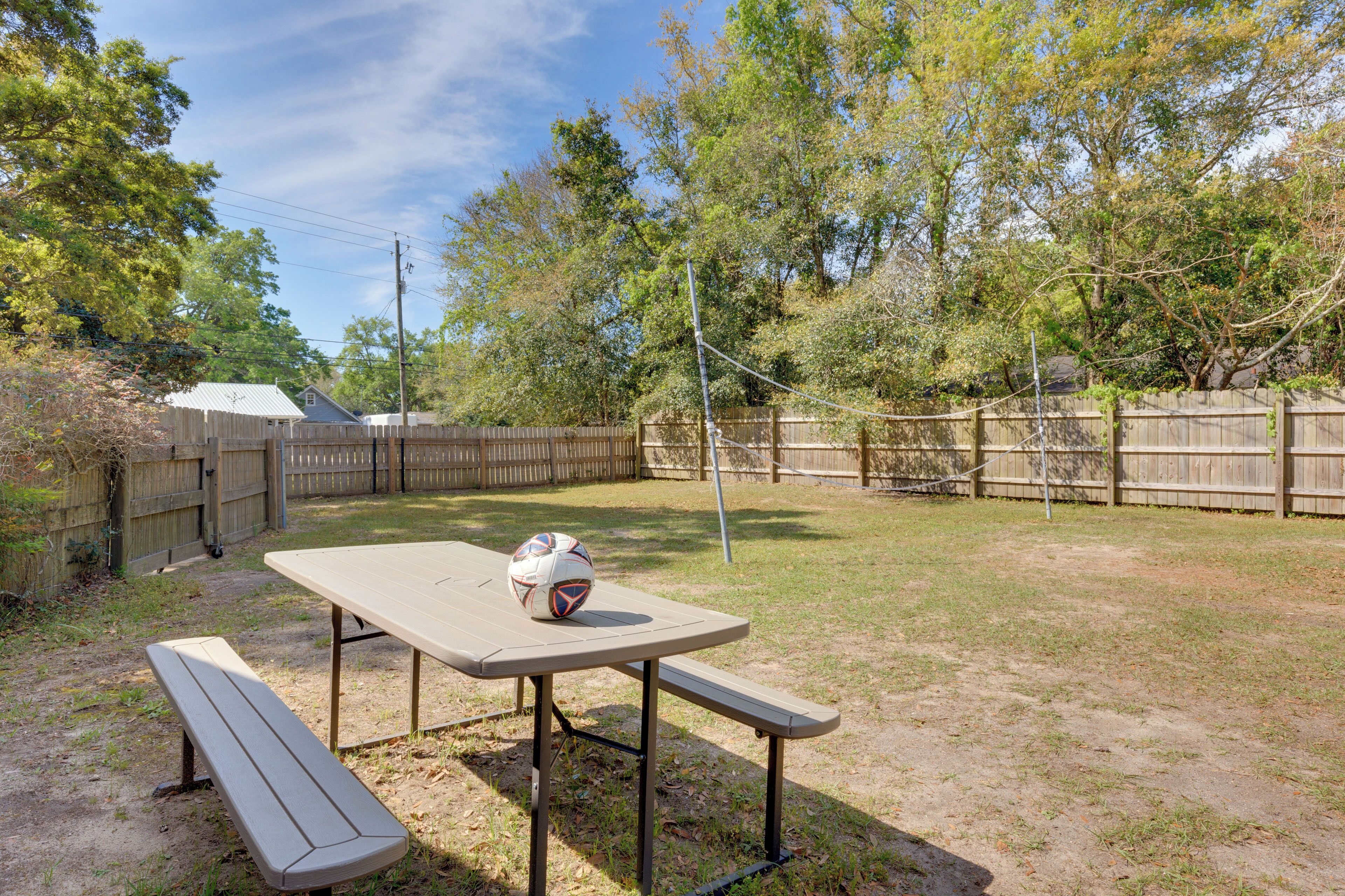 A picnic table with benches and a soccer ball in a backyard with a wooden fence and trees.