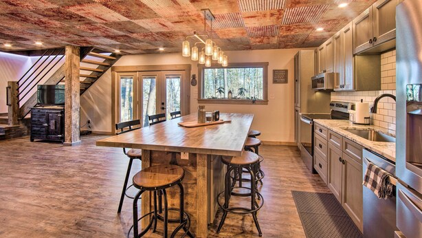 A spacious kitchen with a large island, bar stools, stainless steel appliances, and a rustic ceiling. - 'timberland Estates' Cabin: Close to Trails! (Reedsville)