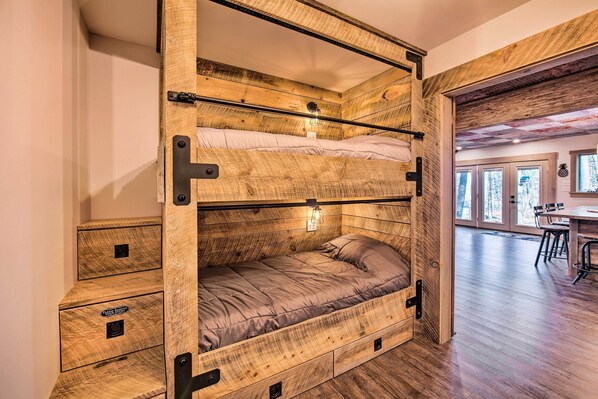 Cama litera con cajones de almacenamiento y espacio de escritorio en una habitación con piso de madera y ventanas amplias.