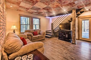 Una sala de estar acogedora con chimenea, un sofá y un ventanal con vistas a un bosque.