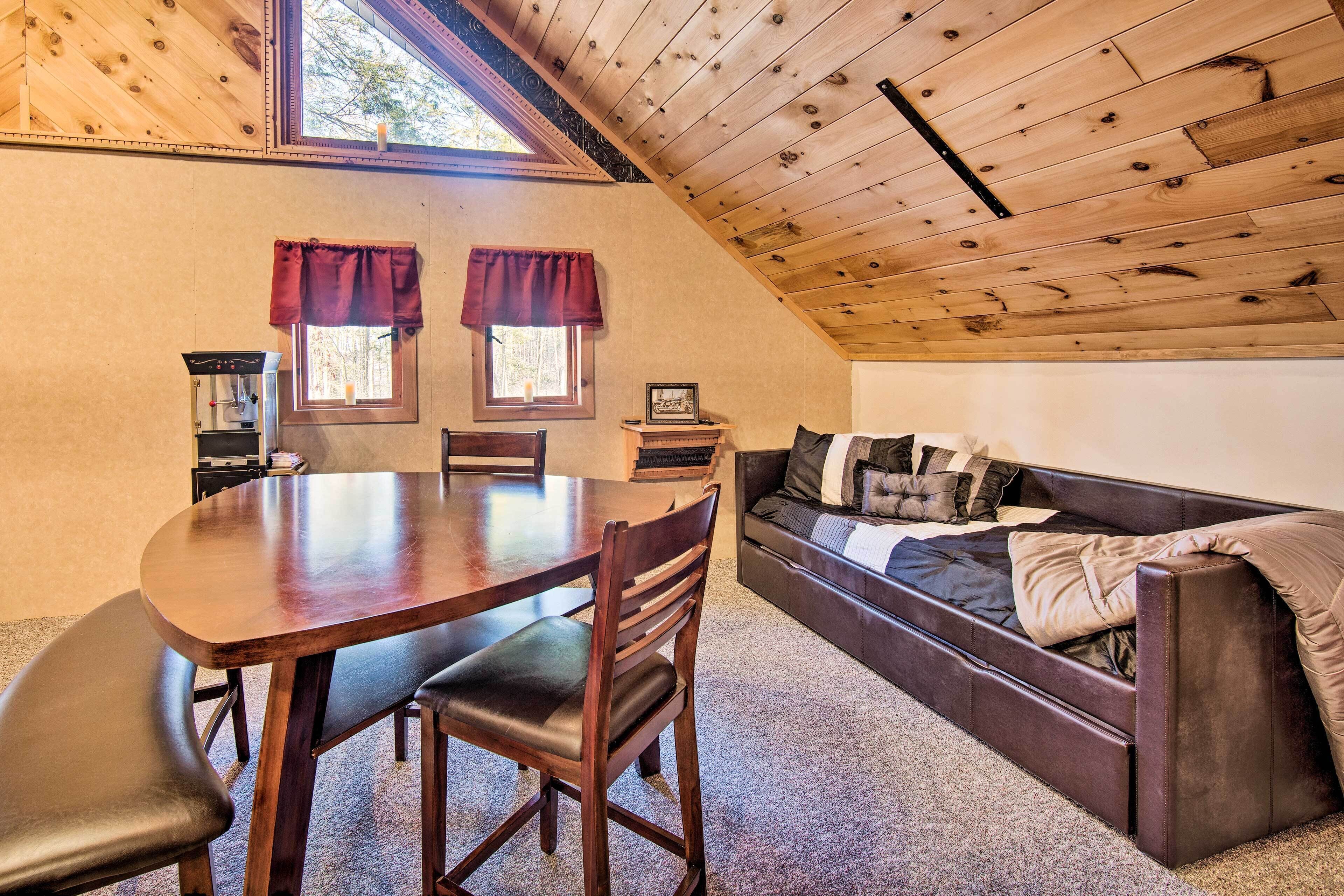 A cozy loft-style room with a wooden ceiling, a dining table with chairs, a sofa, and a window with curtains.