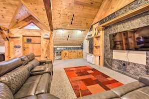 Un intérieur de chalet chaleureux avec un plafond en bois, une cheminée, un coin cuisine et des sièges en cuir.