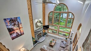 A spacious living area with a fireplace, large windows offering a forest view, and a cozy seating arrangement. - Pocono Lake Paradise w/ Private Beach & Dock! (Pocono Lake)