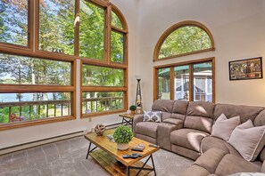 A living room with large windows, a brown leather sofa, a wooden coffee table, and a view of trees and a lake.
