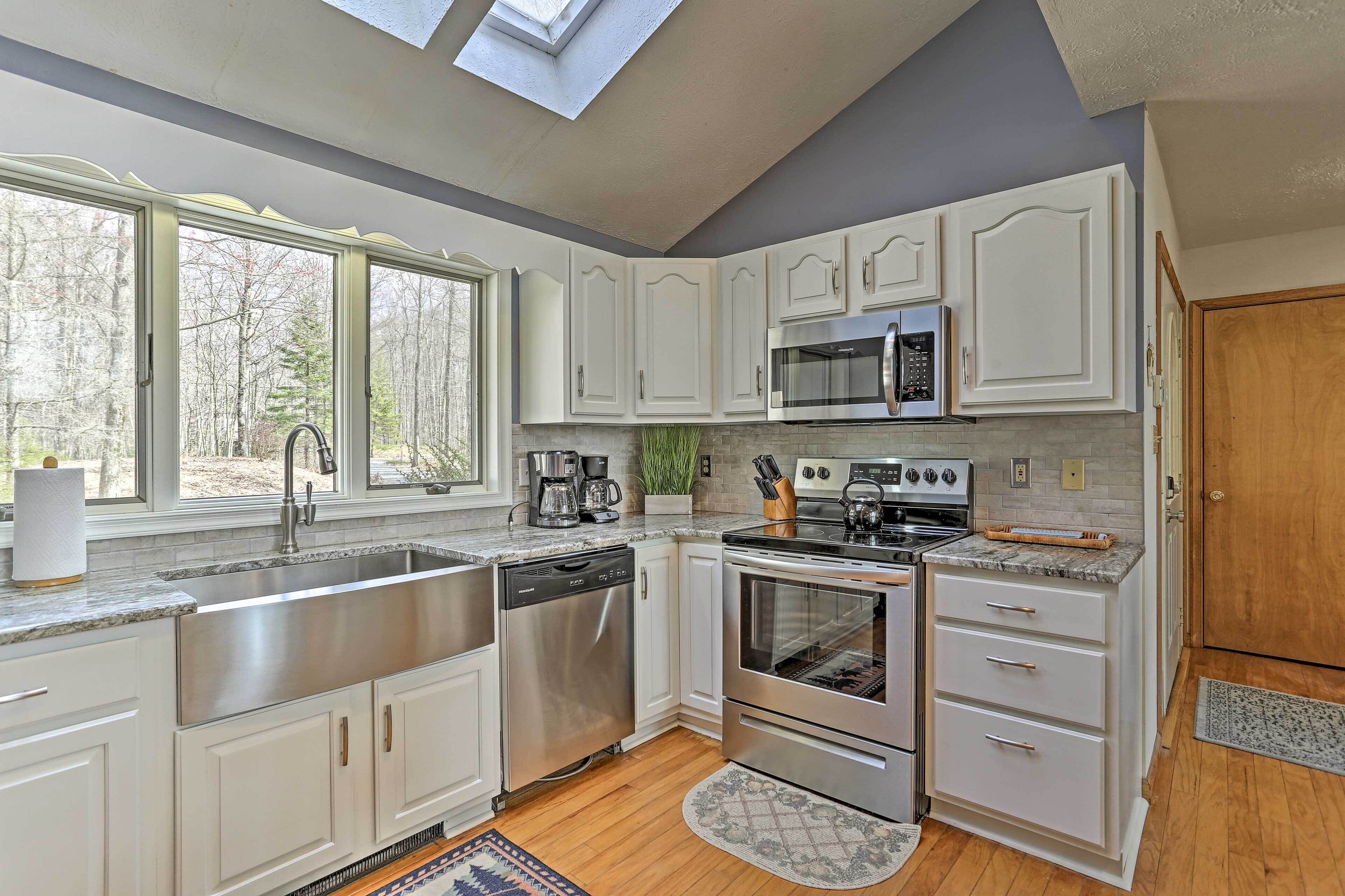 A modern kitchen with white cabinets, stainless steel appliances, and a skylight.