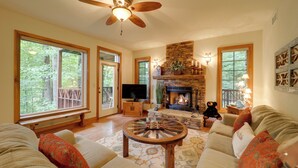 A cozy living room with a fireplace, comfortable seating, and large windows offering a view of the outdoors.