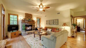 A cozy living room with a fireplace, a comfortable sofa, a television, and a ceiling fan.