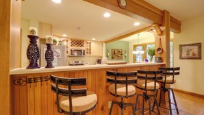 A kitchen with wooden cabinets, a microwave, and a bar area with stools.