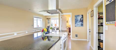 A kitchen with granite countertops, a built-in oven, and a stainless steel range hood. There is a large window providing natural light, and a door leading to another room.