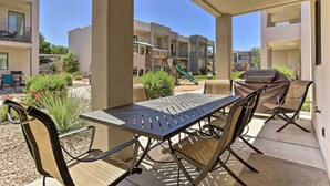 Une terrasse extérieure avec une table et des chaises, un barbecue et, au fond, un espace de jeux pour enfants.
