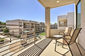 A balcony with a table and chairs, overlooking a courtyard with a pool and greenery. - Sunny Resort Townhome + Balcony & Pool Access (St. George)