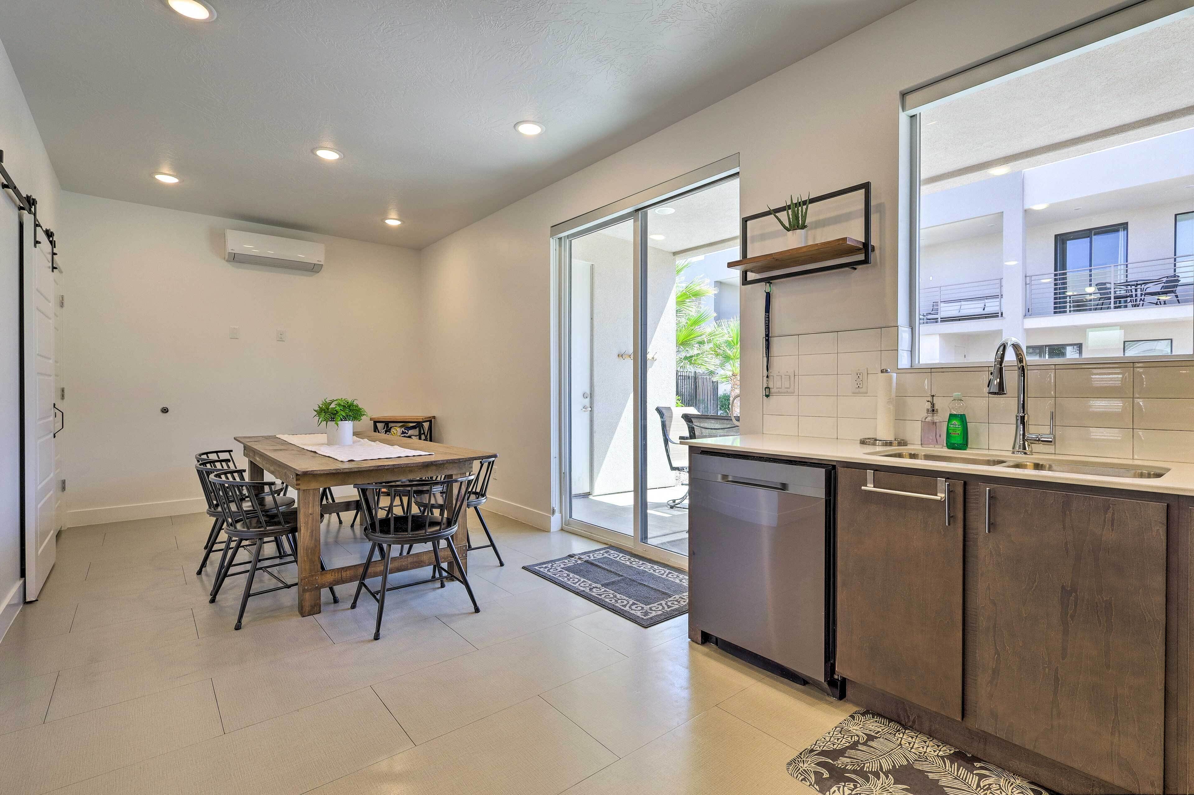 A modern kitchen with a dining area, featuring a large window, a dishwasher, and a built-in oven.