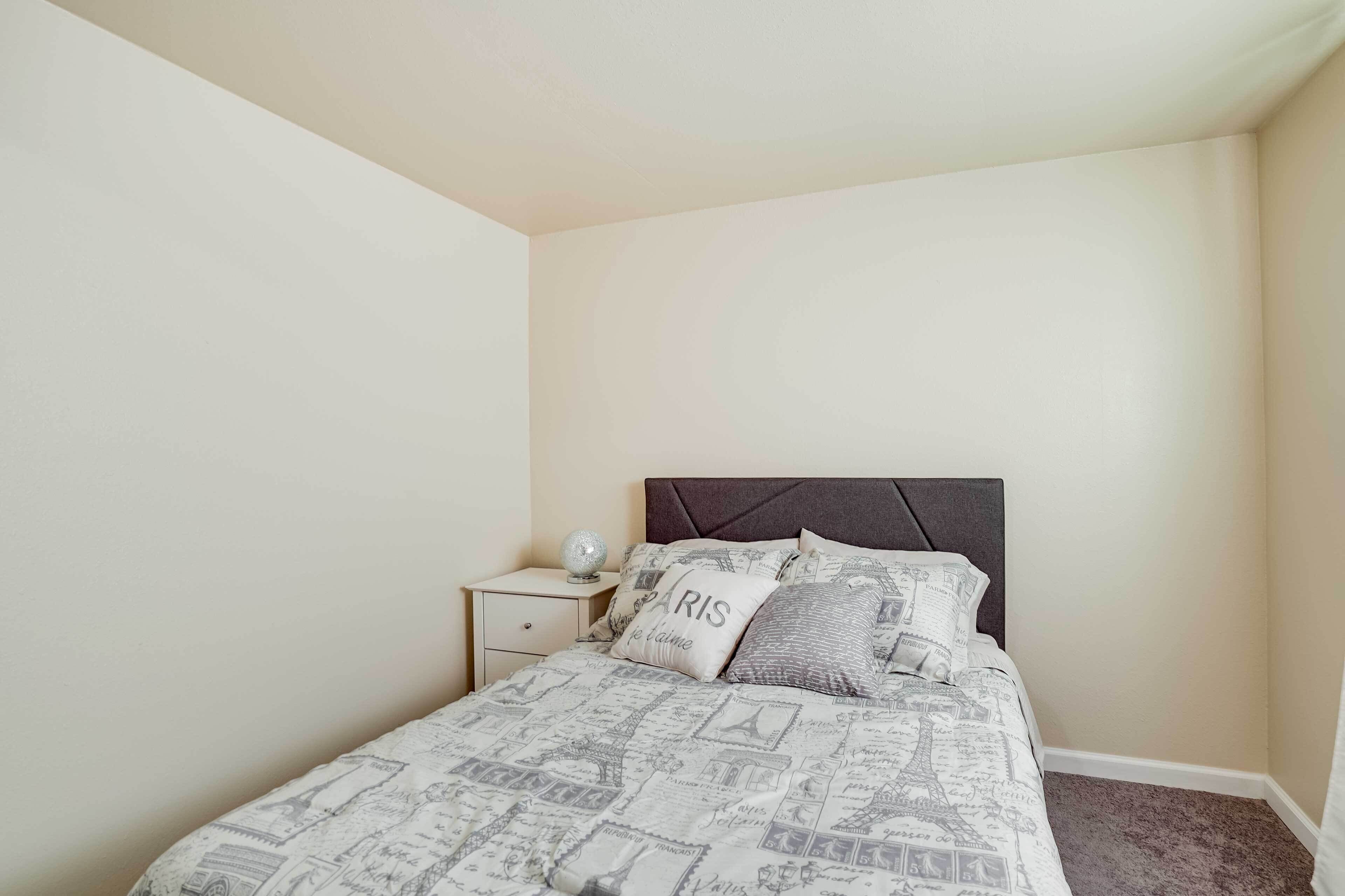 A bedroom with a bed featuring a Paris-themed bedspread, a nightstand with a globe, and a headboard with a diamond pattern.