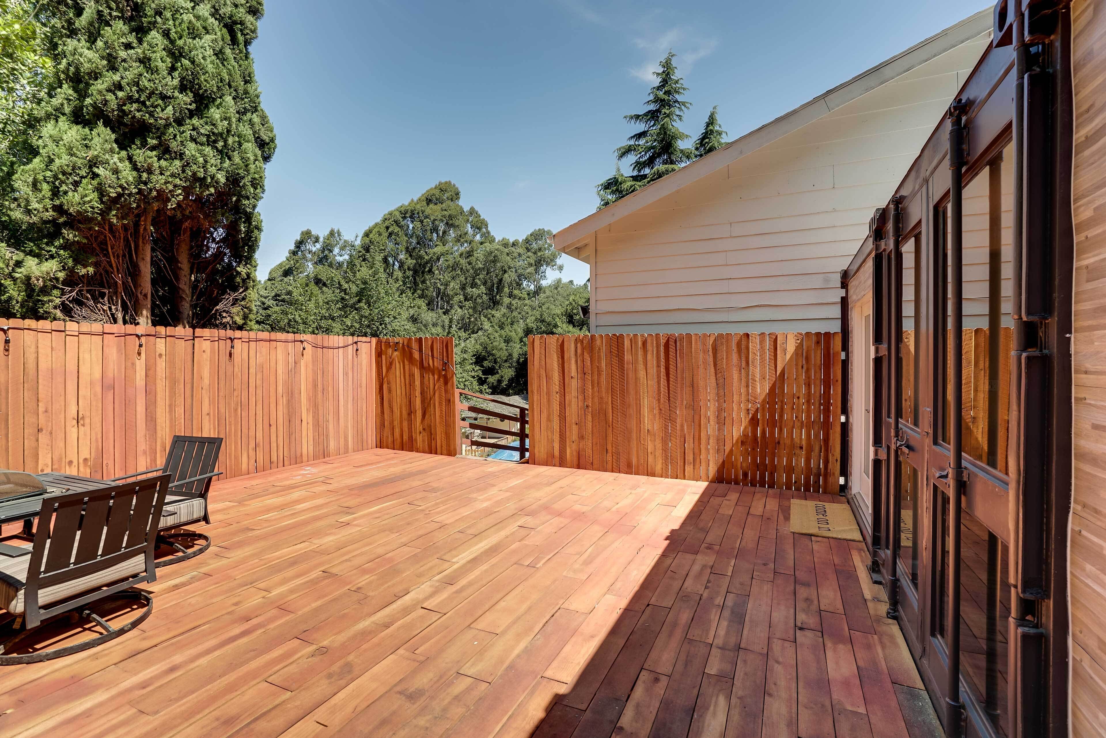 Un patio in legno con un tavolo e sedie, circondato da una recinzione di legno e un edificio con ampie finestre.