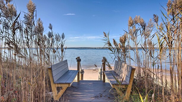 A wooden pier leading to a sandy beach with tall grasses and a clear view of the water. - Waterfront Home w/ Large Deck + Private Pool! (Westhampton Beach)