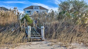 A beach house with a wooden staircase leading to a deck, surrounded by tall grasses. - Waterfront Home w/ Large Deck + Private Pool! (Westhampton Beach)