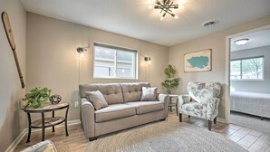 Ein Wohnzimmer mit einem beigefarbenen Sofa, einem gemusterten Sessel, einem kleinen runden Tisch mit einer Pflanze und einem großen Teppich.