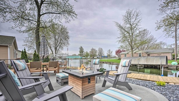 Eine Terrasss mit Adirondack-Stühlen, einer Feuerstelle und Blick auf einen See und Steg.