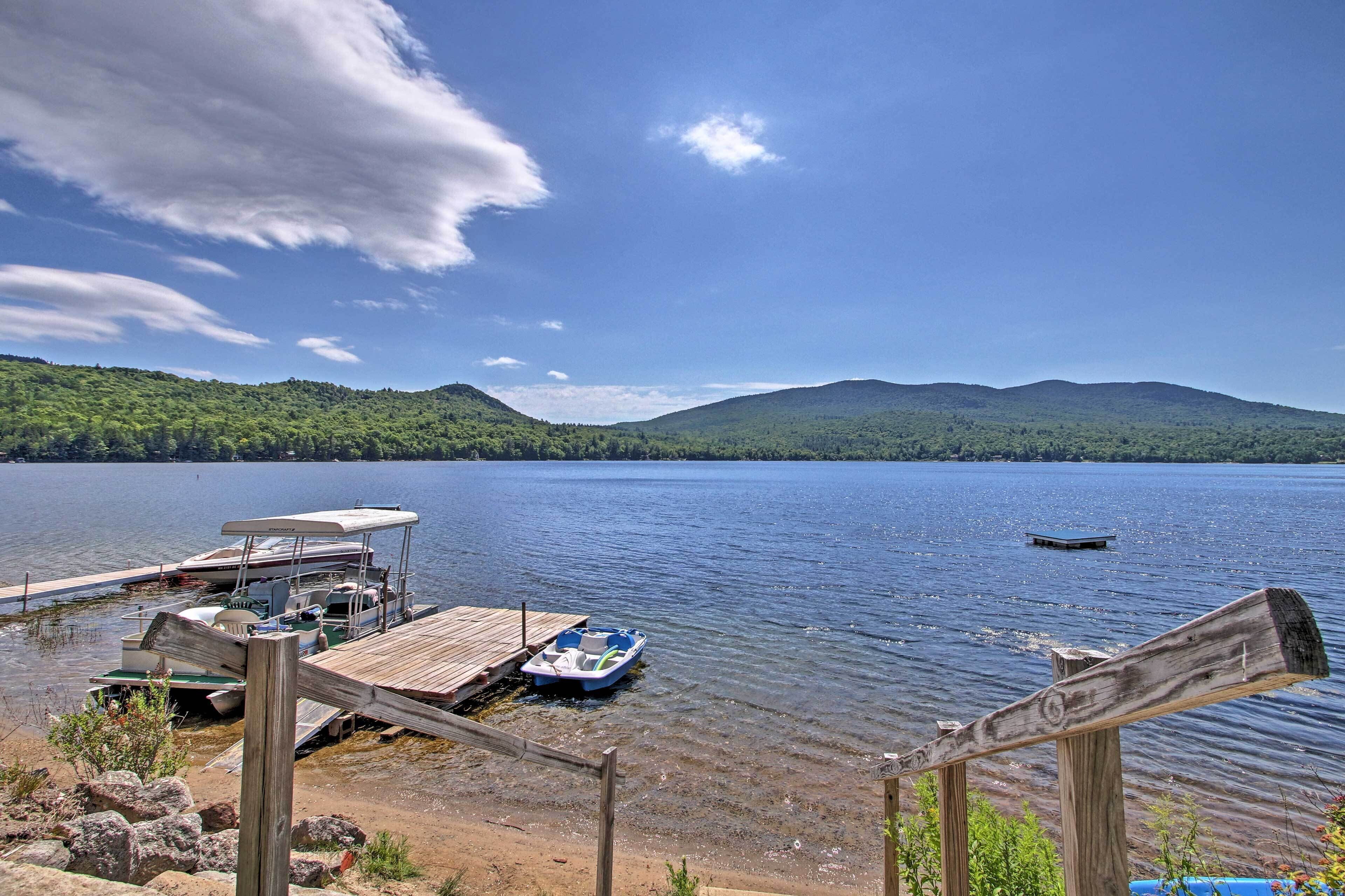 A lakeside dock with boats, a wooden pier, and a forested hill in the background.