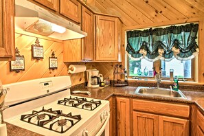 Une cuisine avec des meubles de rangement en bois, une cuisinière à gaz, un évier et une fenêtre avec des rideaux.