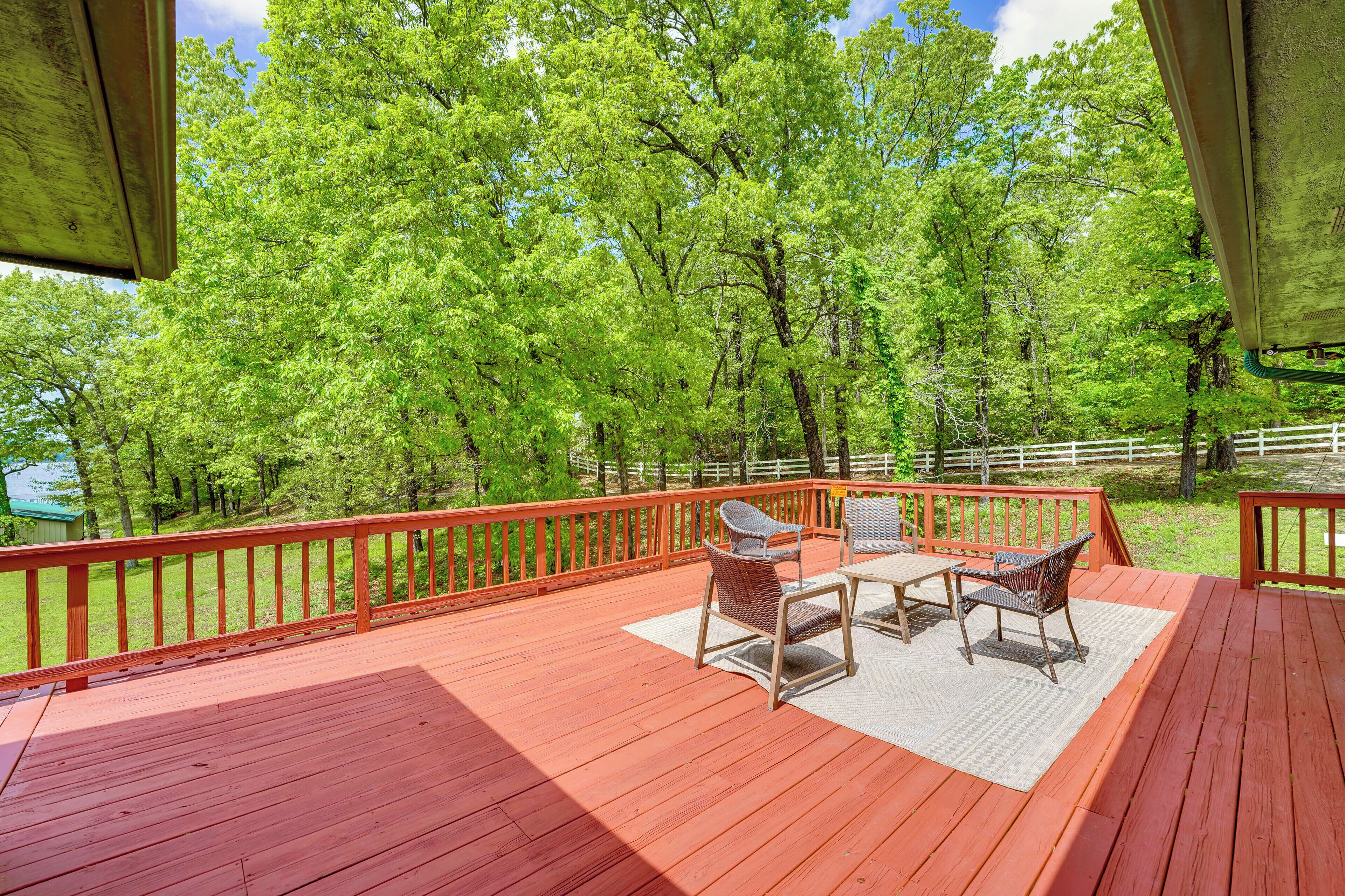 A wooden deck with outdoor furniture, surrounded by a white fence and trees.