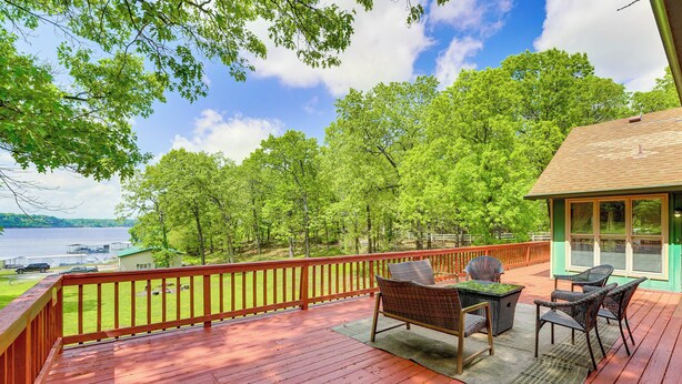 Une terrasse en bois avec des meubles d’extérieur, une vue sur les arbres et un plan d’eau.