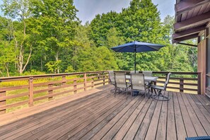 Une terrasse en bois avec une table et des chaises, un parasol et une vue sur une zone boisée.