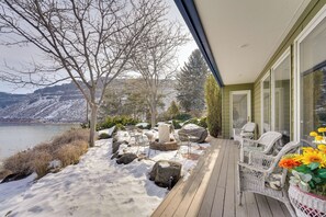 Terraza de madera con mobiliario exterior, vista a un lago y suelo cubierto de nieve.