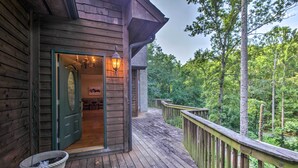 A wooden deck with a green door leading to an interior room, surrounded by a forested area. - Tryon House w/ Hot Tub - Near Equestrian Centers! (Tryon)