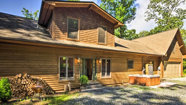 A two-story log cabin with a covered porch, a hot tub, and a stack of firewood. - Tryon House w/ Hot Tub - Near Equestrian Centers! (Tryon)