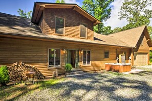 A two-story log cabin with a covered porch, a hot tub, and a stack of firewood. - Tryon House w/ Hot Tub - Near Equestrian Centers! (Tryon)
