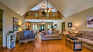 A spacious living room with a high ceiling, wooden balcony, and a fireplace. - Tryon House w/ Hot Tub - Near Equestrian Centers! (Tryon)