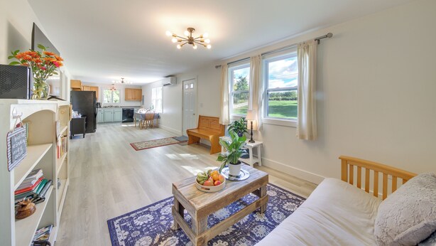 A spacious living area with a wooden coffee table, a sofa, and a dining table with chairs. There is a kitchen in the background with a refrigerator and cabinets. - Woodsy Pittston Retreat Near Kennebec River! (Gardiner)
