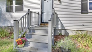 A white house with a front porch, a door, and a small garden with flowers. - Woodsy Pittston Retreat Near Kennebec River! (Gardiner)