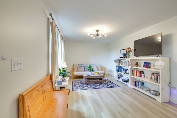 A living room with a wooden bench, a sofa, a coffee table, a bookshelf, and a TV.