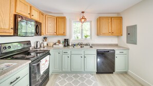A kitchen with wooden cabinets, a stainless steel stove, a dishwasher, and a window with a view of trees. - Woodsy Pittston Retreat Near Kennebec River! (Gardiner)