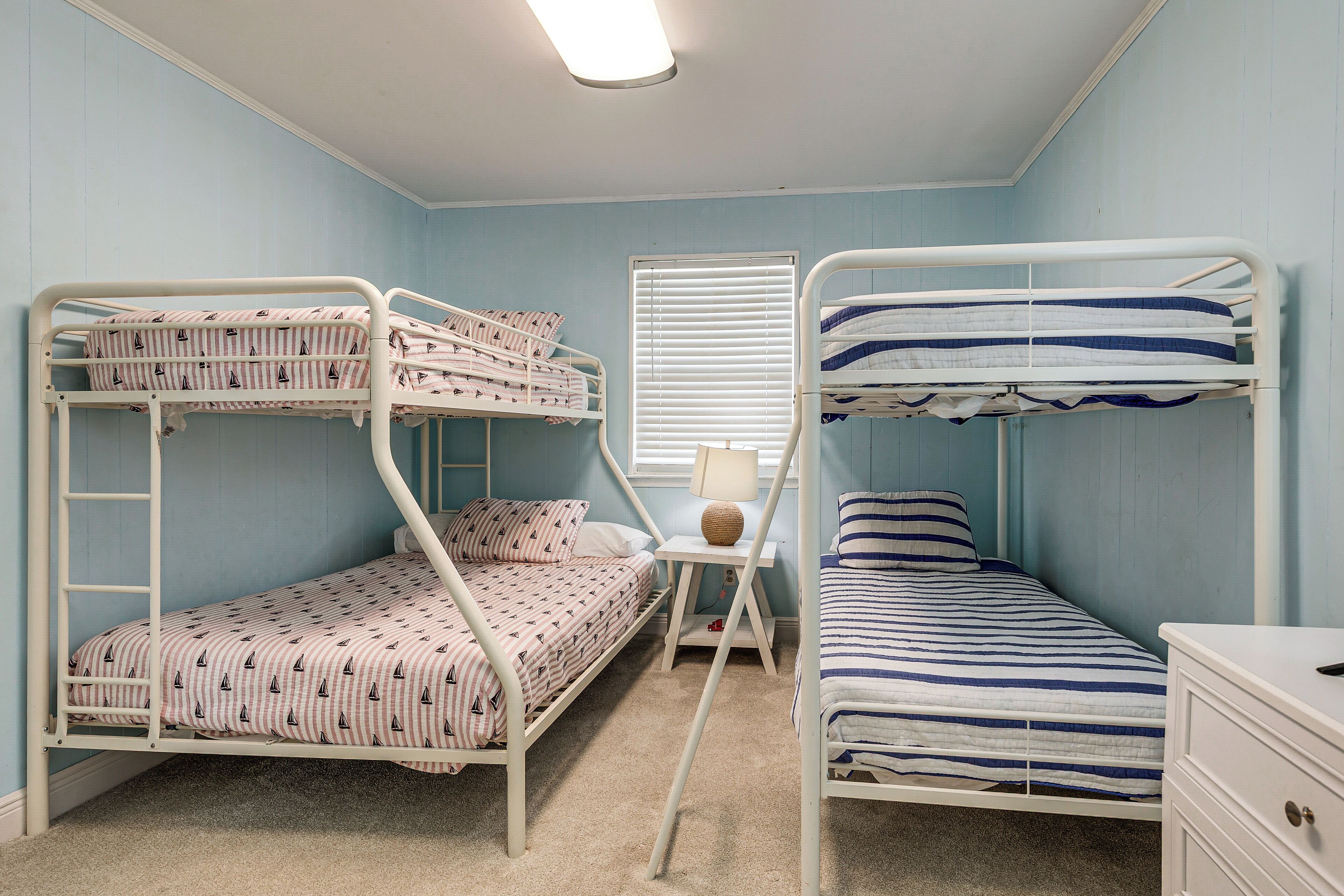 A bunk bed room with a desk and lamp, light blue walls, and a ceiling light.