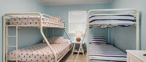 A bunk bed room with a desk and lamp, light blue walls, and a ceiling light.