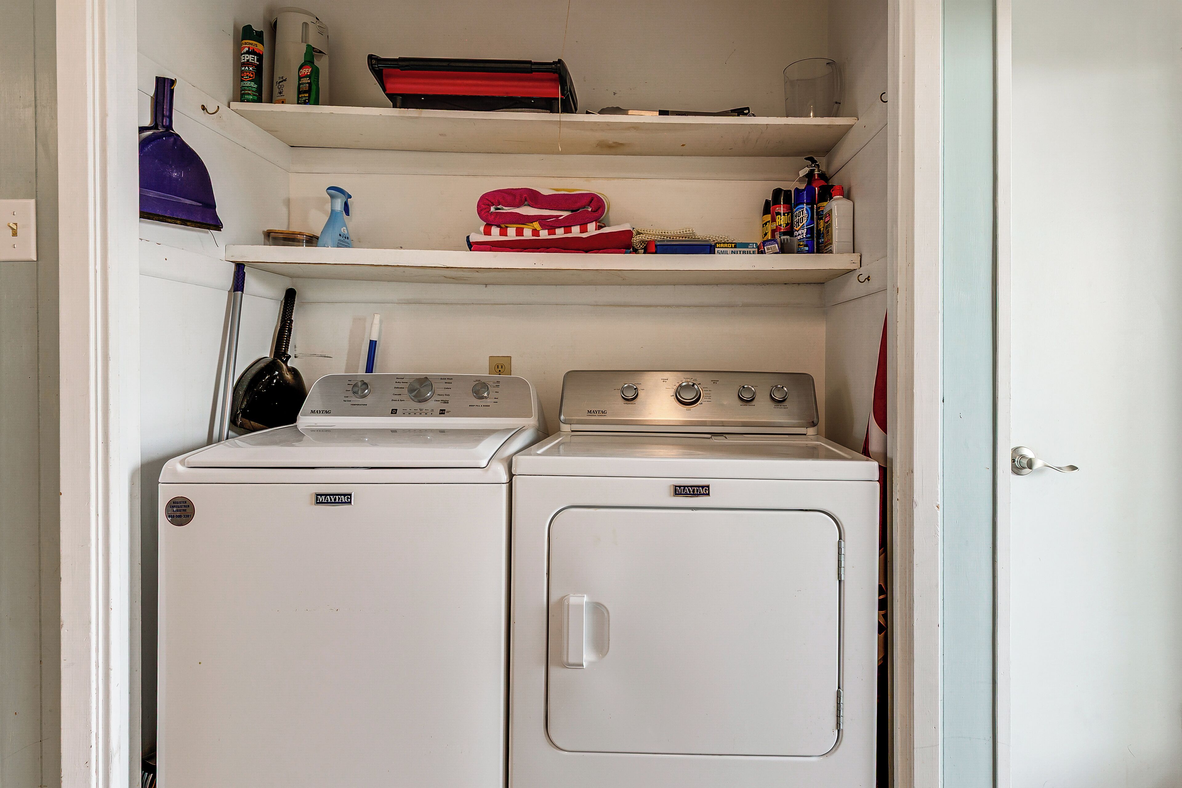 A laundry area with two washing machines, a shelf with cleaning supplies, and a purple mop.